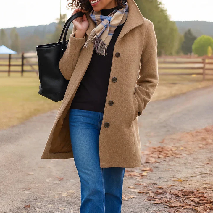 A woman wearing an elegant camel button-through coat over a sweater on a crisp fall day.