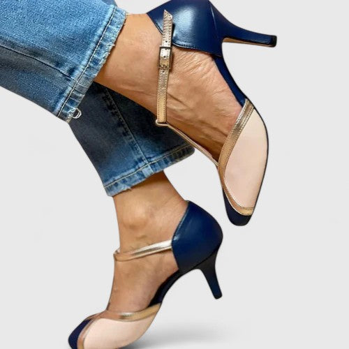 A woman wearing navy, blush and gold T-strap heels with a rounded toe, paired with jeans.