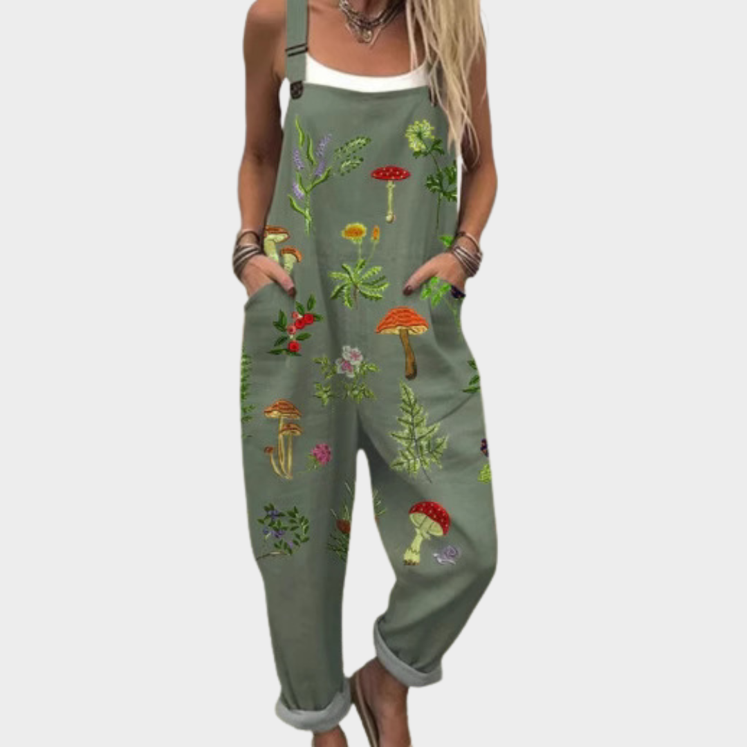 Woman wearing olive green overalls with a botanical mushroom and fern print, adjustable straps, cheerful and relaxed.