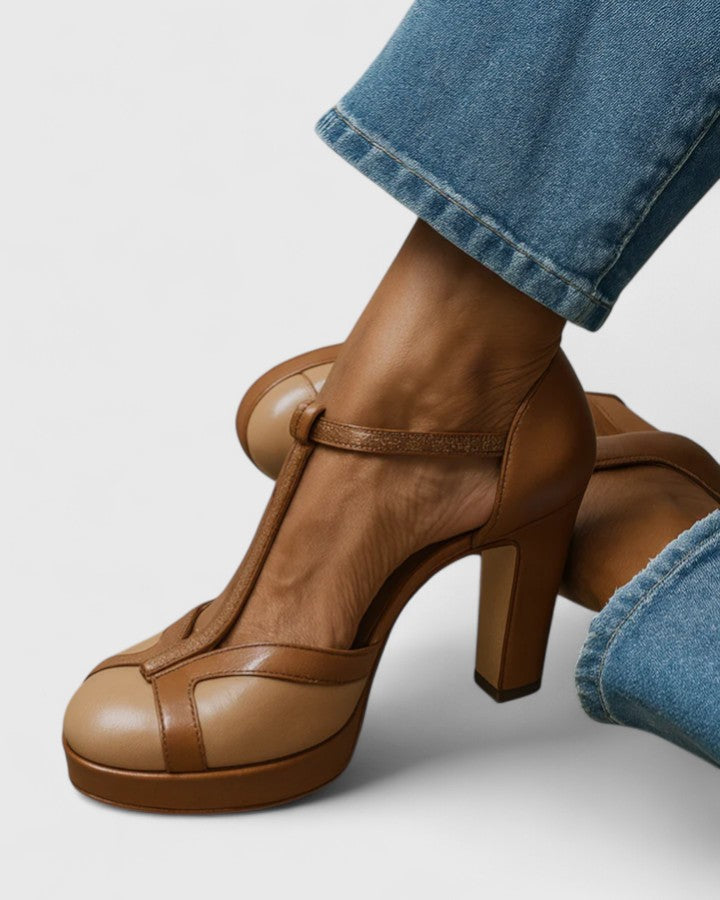 A woman wearing brown round-toe T-strap heels, standing elegantly in a smart outfit.