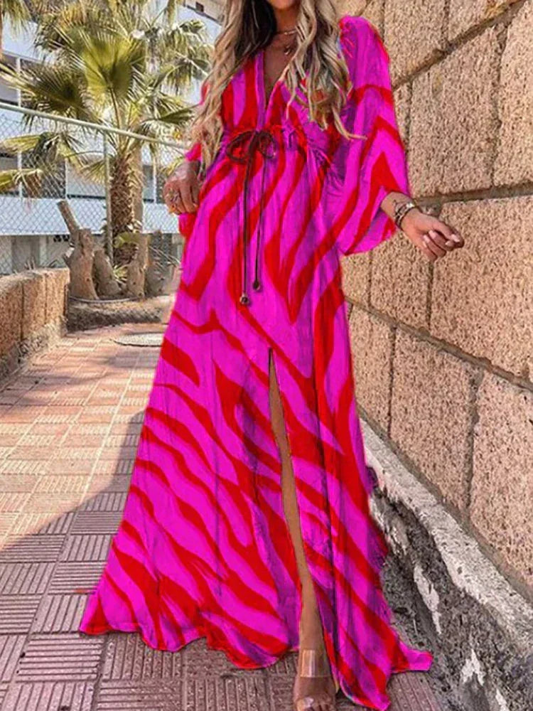 Woman wearing a colourful abstract print kaftan maxi dress with flowing sleeves by the water.