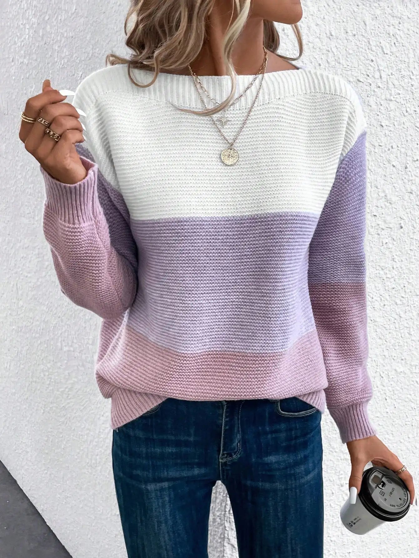 A woman wearing a soft colour block sweater in cream, taupe and beige with a wide boat neckline.