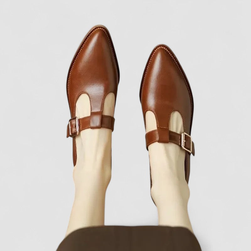 A woman wearing black pointed Mary Jane shoes with an adjustable buckle strap, standing elegantly.