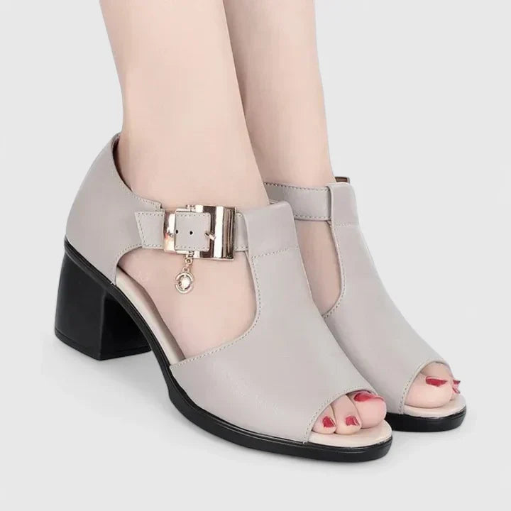 A woman wearing black peep-toe block heels with a T-strap and gold buckle.