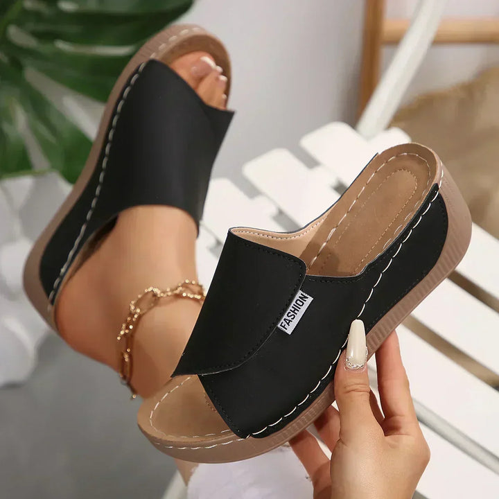 A woman wearing warm tan slide sandals on a sunny seaside walk.