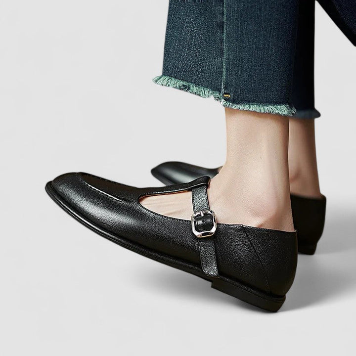 Woman wearing black low-heel Mary Jane shoes with a strap, stepping through a doorway.