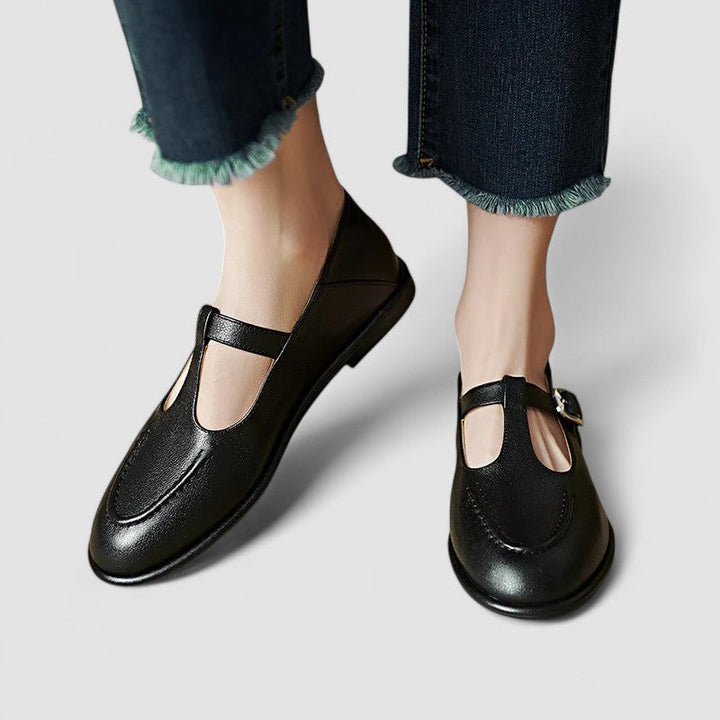 Woman wearing black low-heel Mary Jane shoes with a strap, stepping through a doorway.