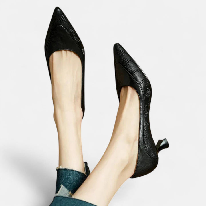A woman wearing black pointed kitten-heel pumps with a subtle embossed finish.
