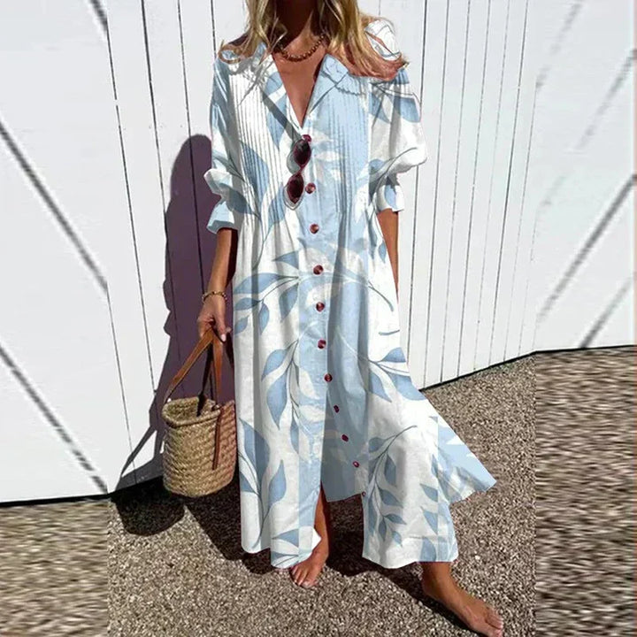 Woman wearing the Gail™ leaf print maxi dress with a button front, walking along the coast in a light breeze.