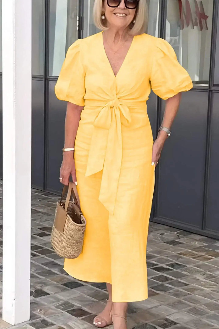 Woman wearing the Christina bow-front midi dress with puff sleeves at a garden party.
