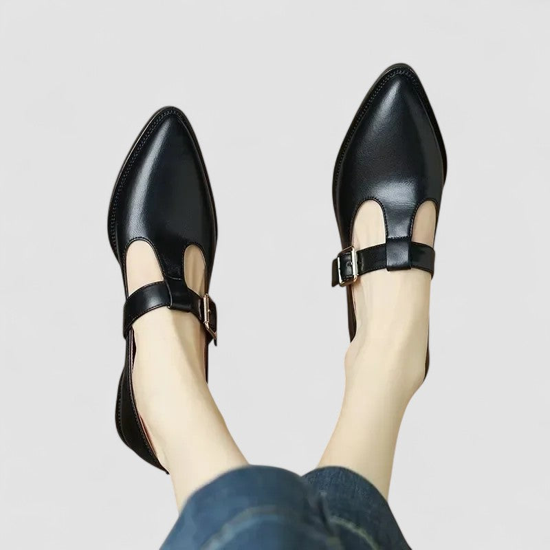 A woman wearing black pointed Mary Jane shoes with an adjustable buckle strap, standing elegantly.
