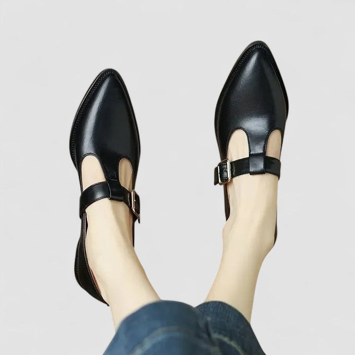 A woman wearing black pointed Mary Jane shoes with an adjustable buckle strap, standing elegantly.