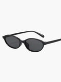 A woman by the sea wearing classic oval vintage sunglasses, relaxed and elegant in the sun.