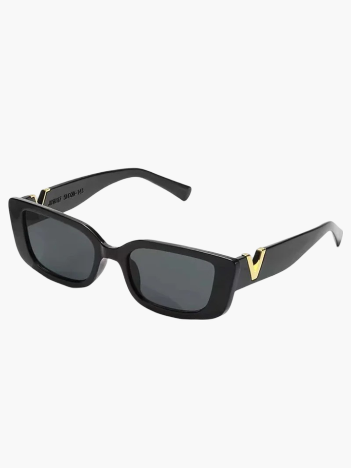 A woman at an outdoor event wearing chunky black rectangular retro sunglasses with a gold-tone accent.