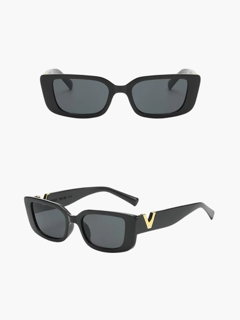 A woman at an outdoor event wearing chunky black rectangular retro sunglasses with a gold-tone accent.