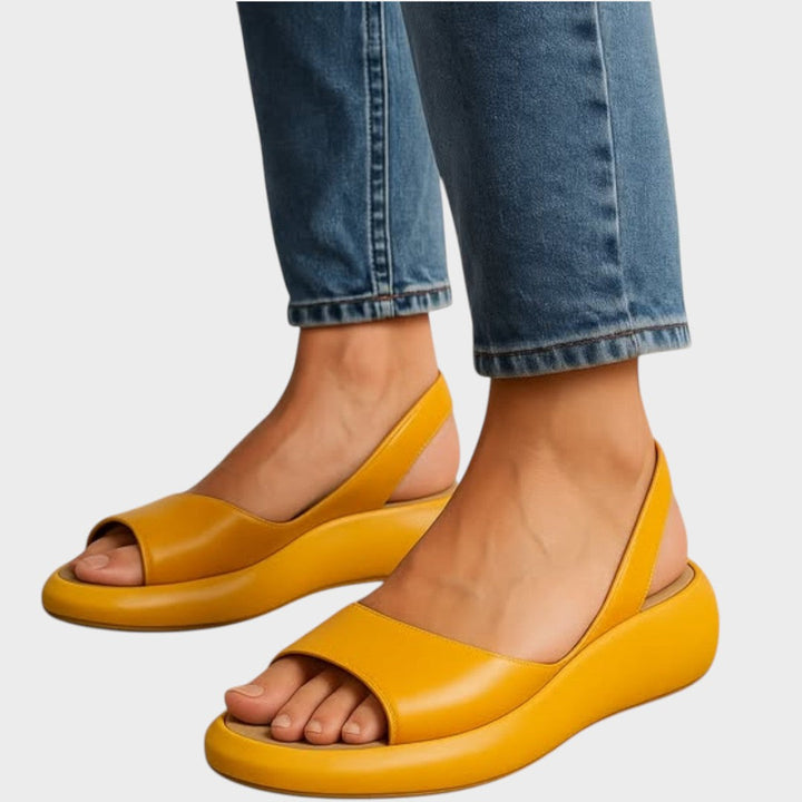 A woman walking gracefully in lightweight orthopaedic sandals with an adjustable strap on a sunny day.