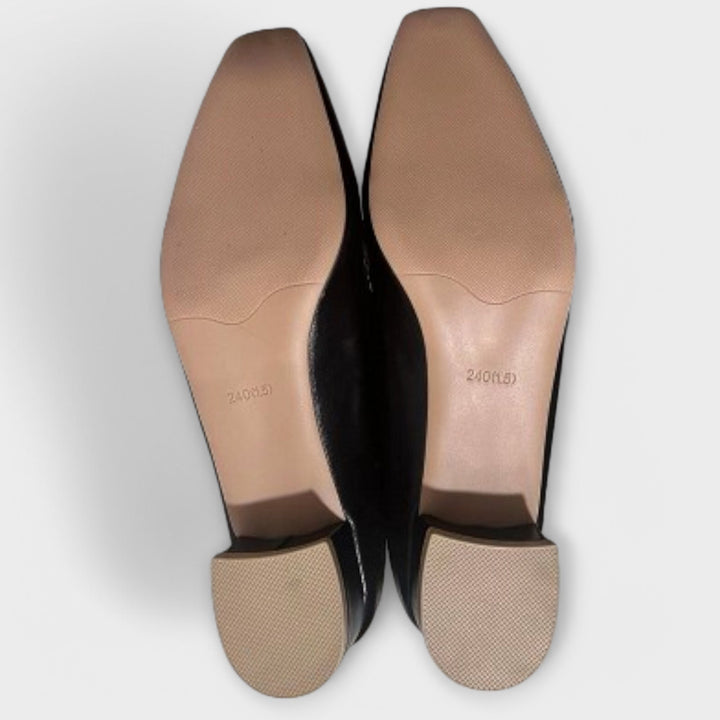A pair of soft beige square-toe loafers with a chain-link ornament across the front.