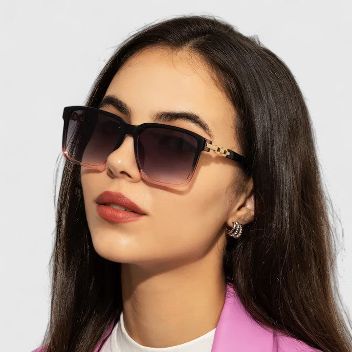 A woman by the pool wearing bold square sunglasses with chain-detail temples, confident in the sun.