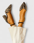 A woman wearing zebra-print block heels with a pointed toe, open sides and a slim ankle strap.