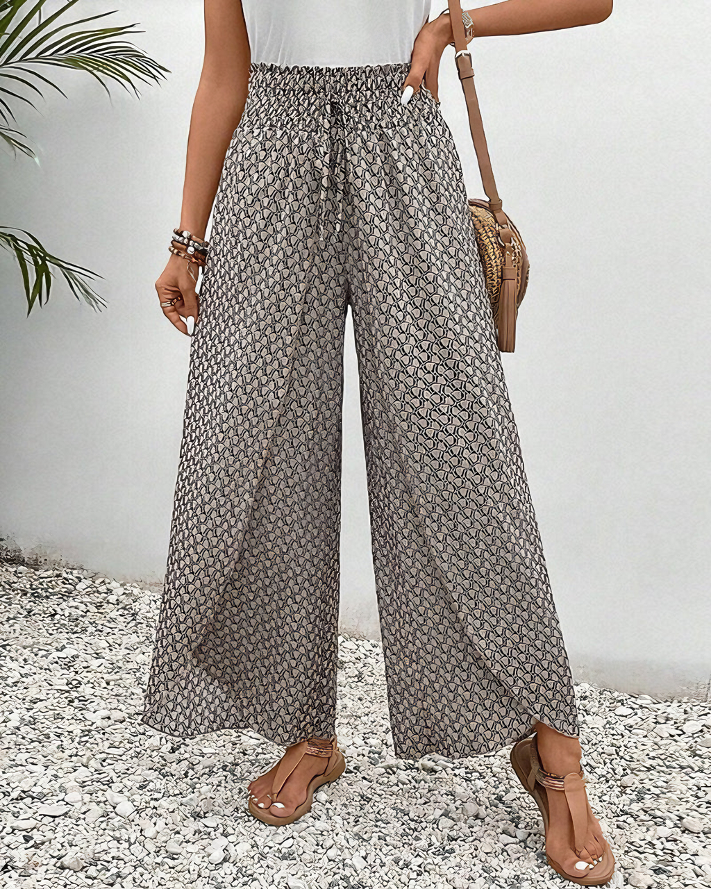 A woman wearing wide, flowing pants in a beige-and-black geometric print with an elastic drawstring waist.