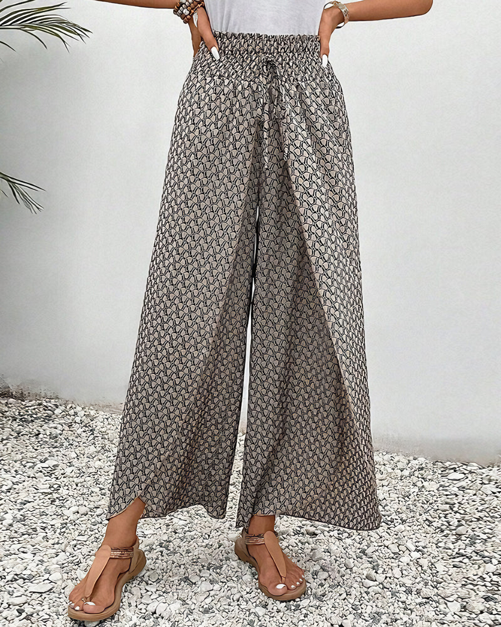 A woman wearing wide, flowing pants in a beige-and-black geometric print with an elastic drawstring waist.
