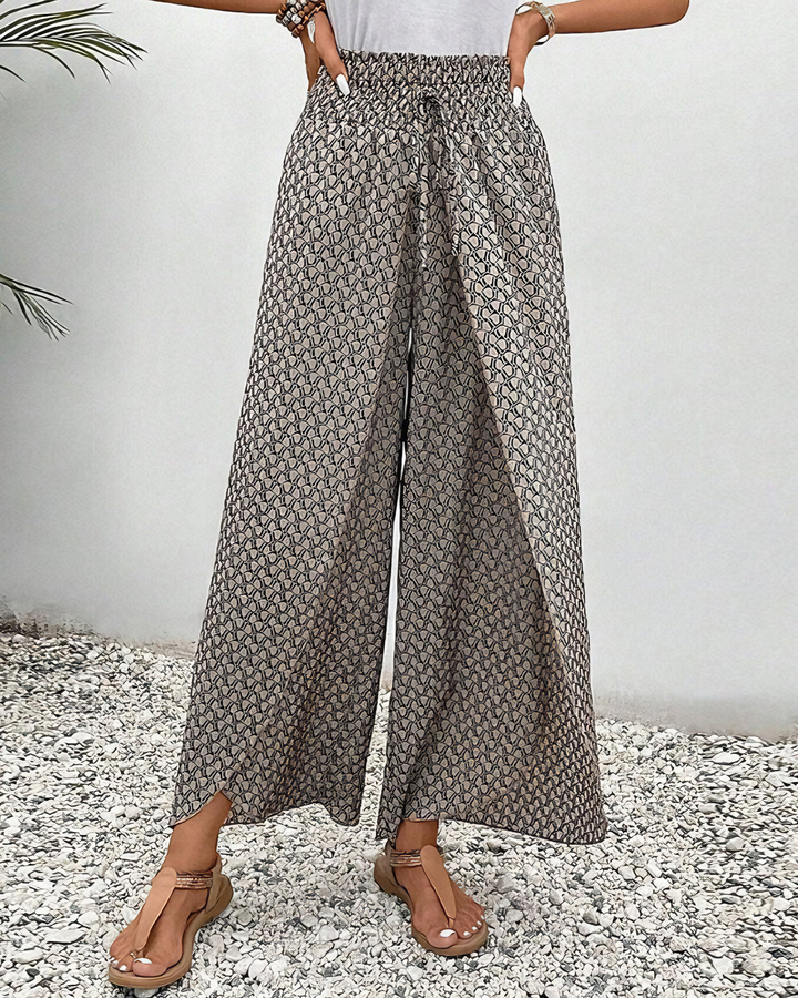 A woman wearing wide, flowing pants in a beige-and-black geometric print with an elastic drawstring waist.