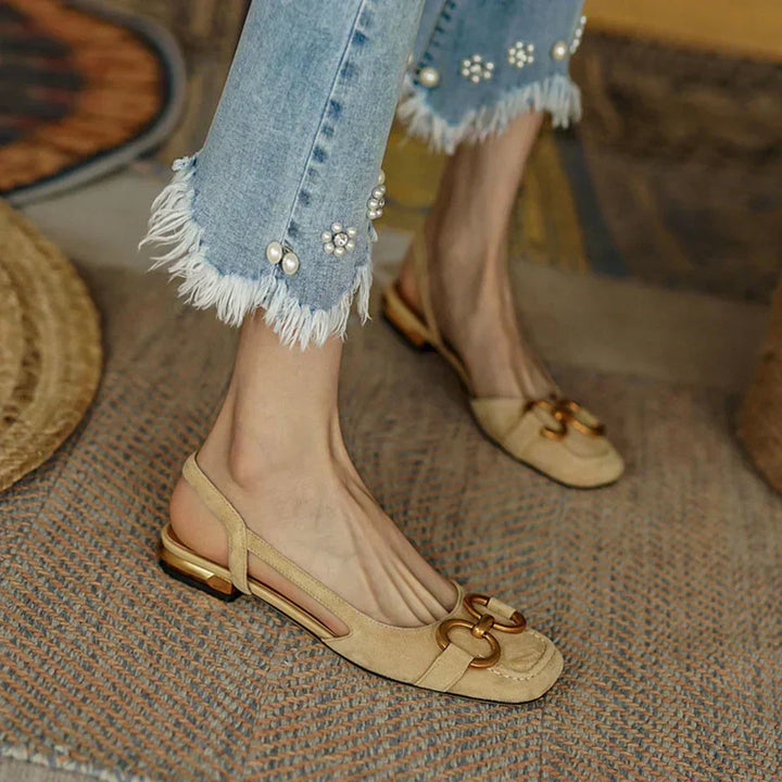 A woman wearing navy square-toe open-back flats with a small golden buckle detail.