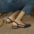 A woman wearing navy square-toe open-back flats with a small golden buckle detail.