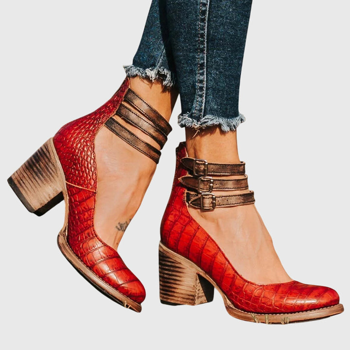A woman wearing tan block-heel court shoes with buckled ankle straps, walking gracefully in a refined outfit.