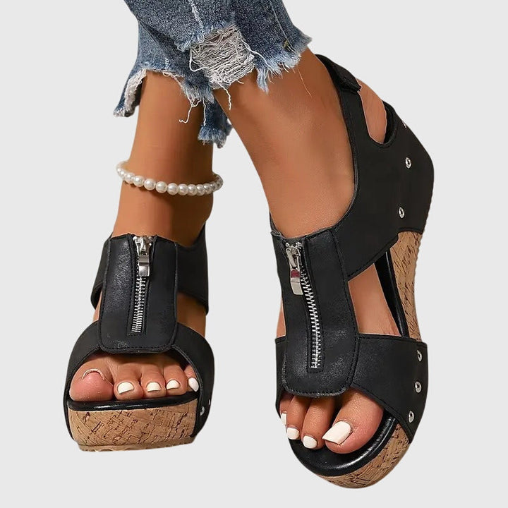 A woman wearing black zip-front wedge sandals with a cushioned footbed and open toe.