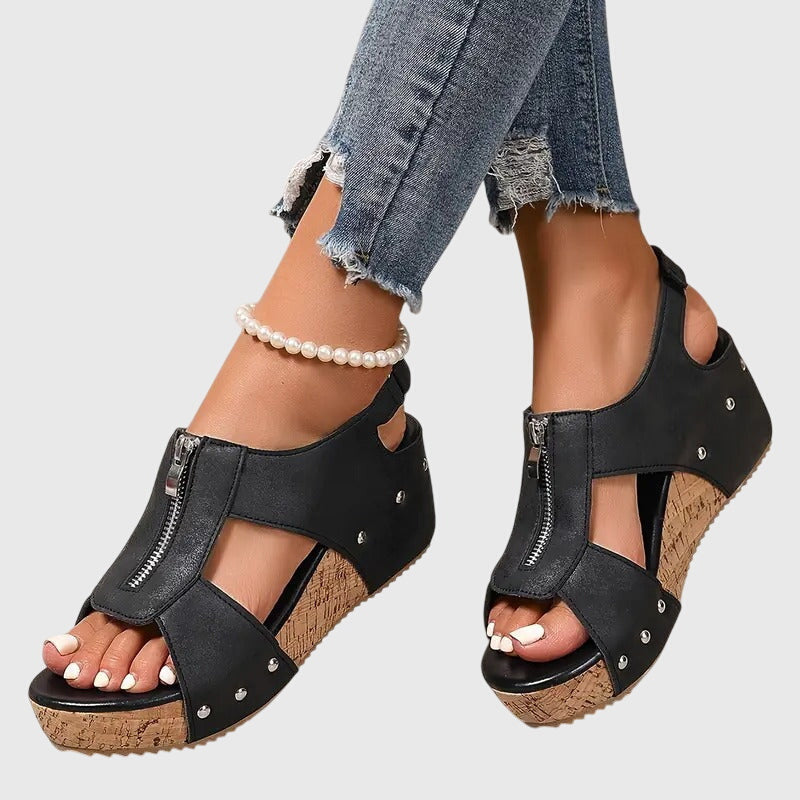 A woman wearing black zip-front wedge sandals with a cushioned footbed and open toe.
