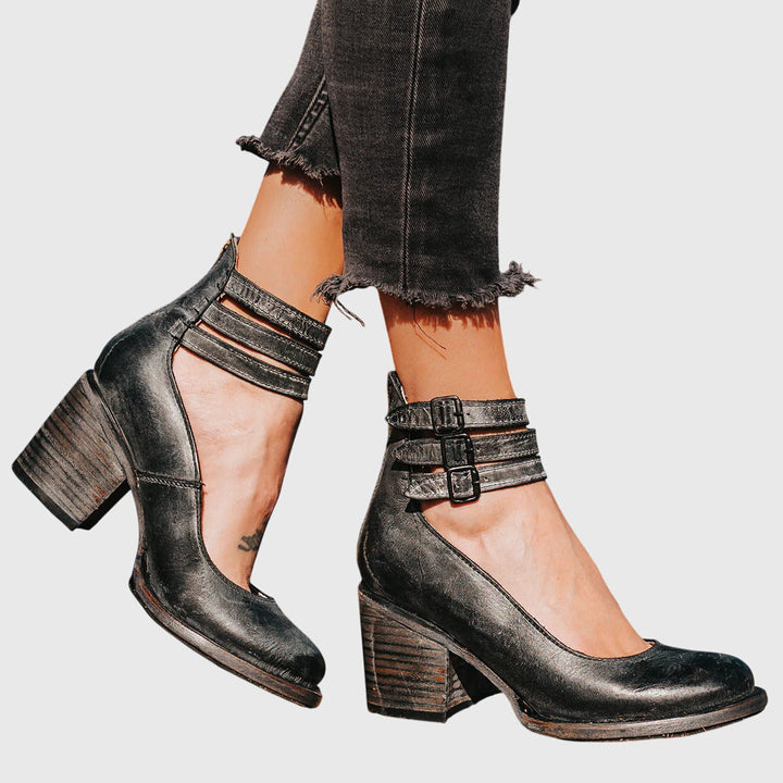 A woman wearing tan block-heel court shoes with buckled ankle straps, walking gracefully in a refined outfit.