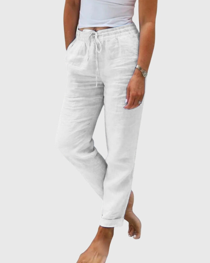 Woman wearing tailored pants with a smart top, standing confidently in soft light.