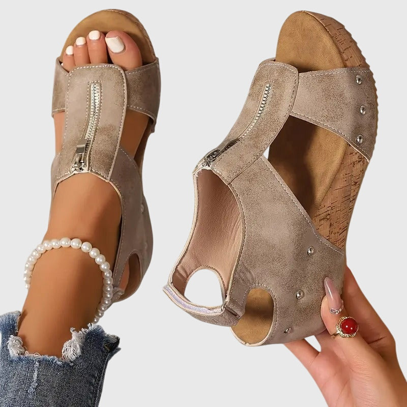 A woman wearing black zip-front wedge sandals with a cushioned footbed and open toe.