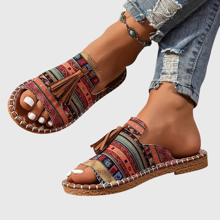 A woman wearing colourful patterned boho slides with tassel details on a holiday day out.