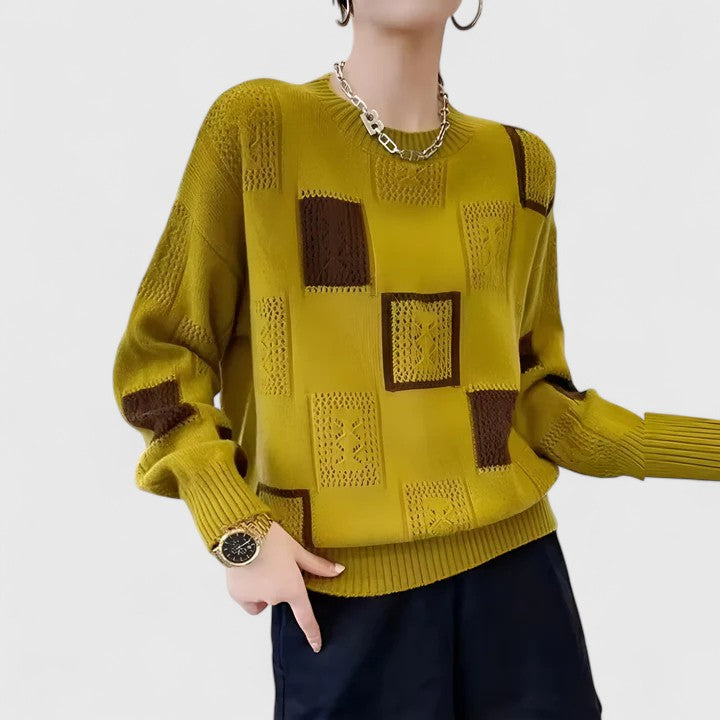 A woman wearing a white sweater with black geometric squares and openwork detailing, round neck.