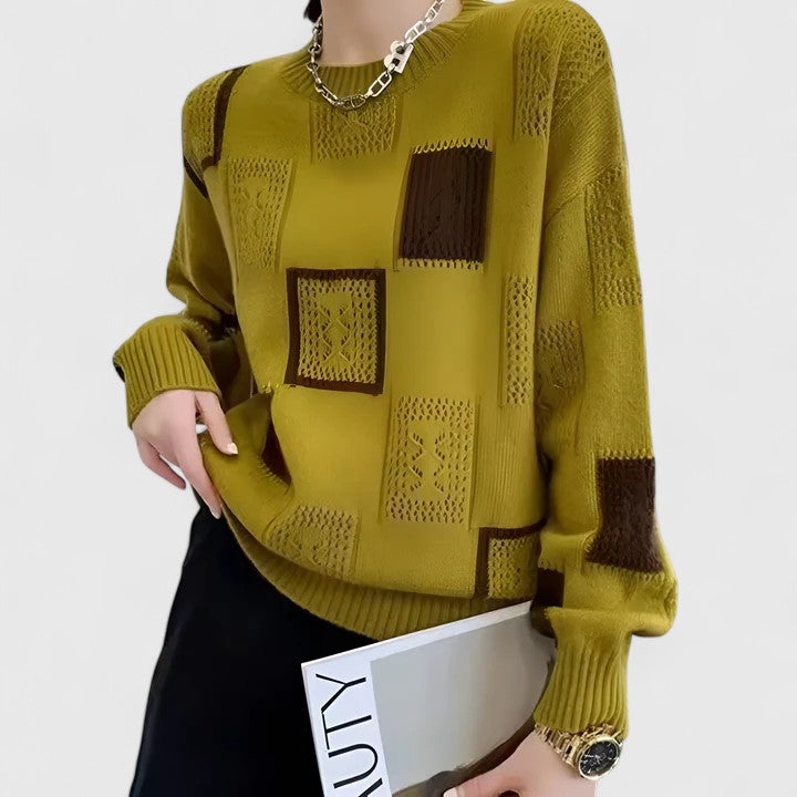 A woman wearing a white sweater with black geometric squares and openwork detailing, round neck.