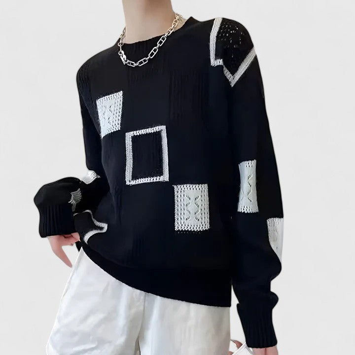 A woman wearing a white sweater with black geometric squares and openwork detailing, round neck.
