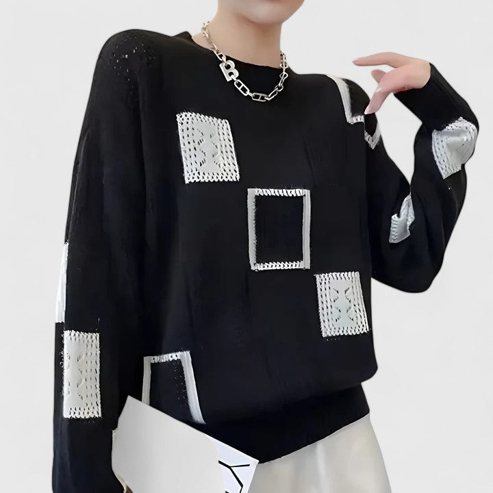 A woman wearing a white sweater with black geometric squares and openwork detailing, round neck.