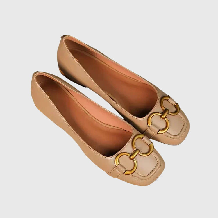 A pair of black slip-on flats with a polished gold ring detail across the toe.