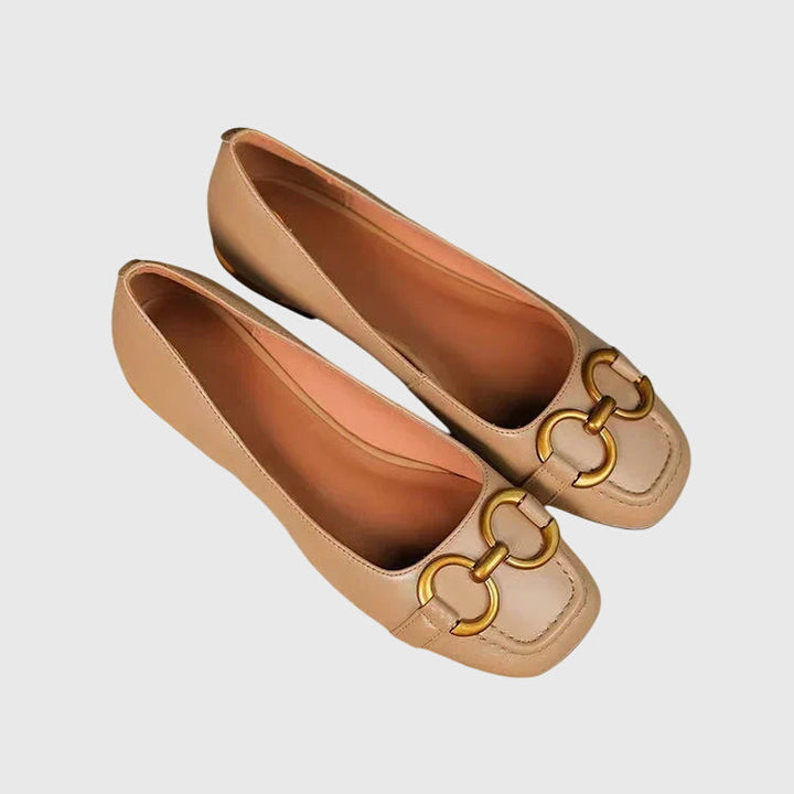 A pair of black slip-on flats with a polished gold ring detail across the toe.