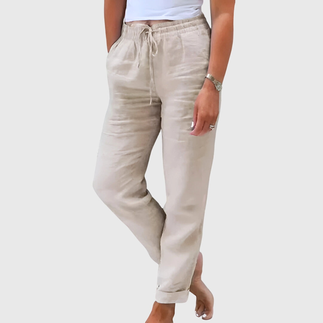 Woman wearing tailored pants with a smart top, standing confidently in soft light.