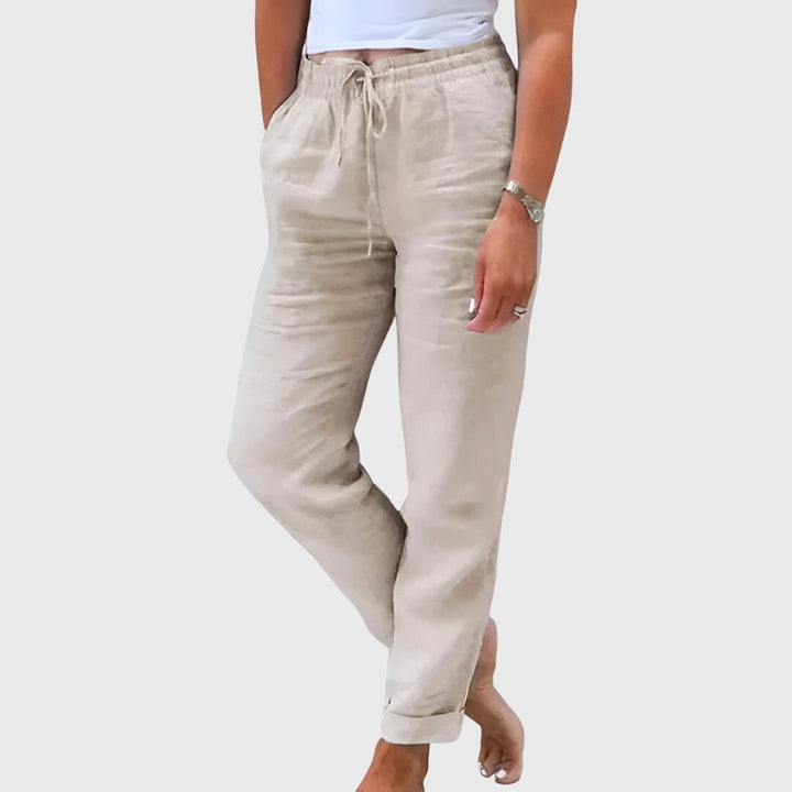 Woman wearing tailored pants with a smart top, standing confidently in soft light.