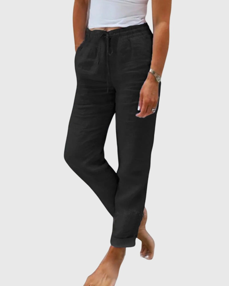 Woman wearing tailored pants with a smart top, standing confidently in soft light.