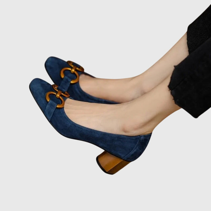 A woman wearing khaki block-heel court shoes with a gold buckle detail, standing with ease and confidence.