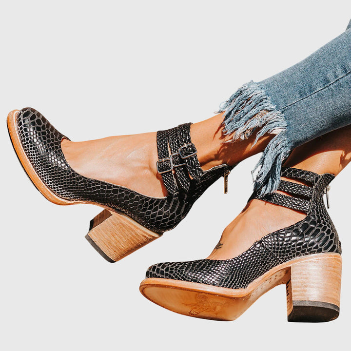 A woman wearing tan block-heel court shoes with buckled ankle straps, walking gracefully in a refined outfit.