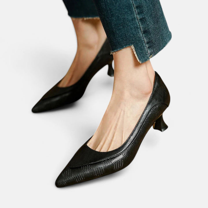 A woman wearing black pointed kitten-heel pumps with a subtle embossed finish.