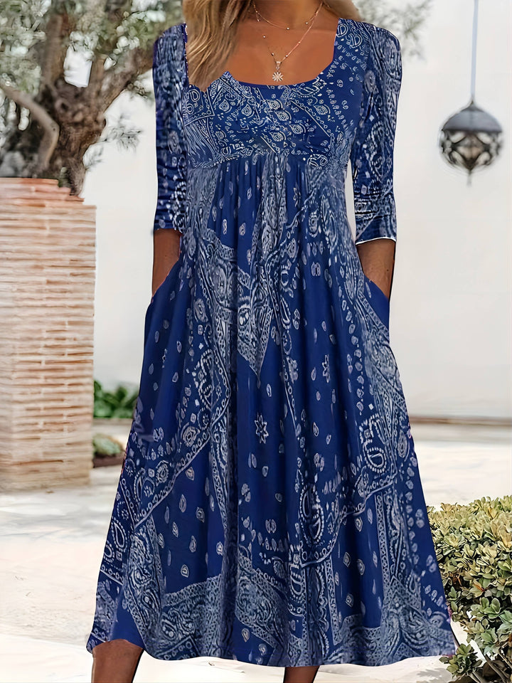 A woman wearing the Maria long sleeve grey paisley midi dress with a square neckline and flowing skirt, styled for a relaxed day out.