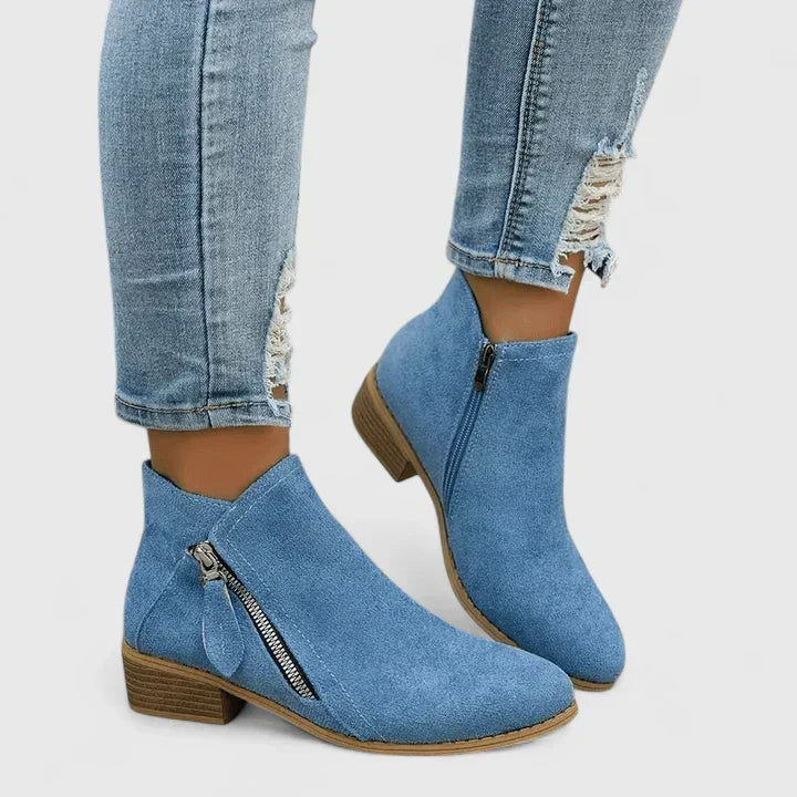 Woman wearing light blue vintage-style ankle boots, walking along a leafy street.