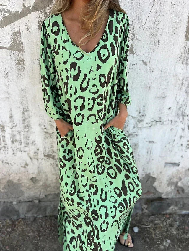 Woman in the Alison leopard print maxi dress with long sleeves and a V-neckline, walking along the shoreline.